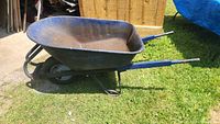 Side profile of blue metal wheelbarrow showing tire, frame and handles