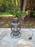 Front view of black metal railroad lantern with cord on tabletop outdoors