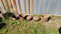 Five rusted cast iron pots with some lids lined up outdoors