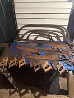 Wide shot of all saws laid on table: seven panel saws, four bow saw frames, one hacksaw