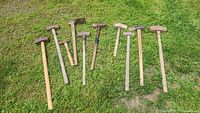 Group photo of ten wooden-handle sledge hammers laid on grass