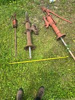 Overview of three antique well pumps laid out on grass with measuring tape for scale