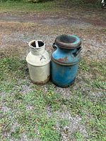 Blue and cream metal milk cans standing side by side on gravel