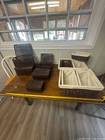 Tabletop view showing all eleven brown wicker baskets including eight open baskets of varying sizes and three white-lined baskets