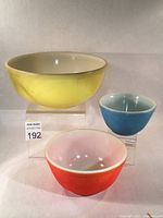 Set of three vintage Pyrex mixing bowls in yellow, blue, and red arranged with yellow bowl largest in rear and blue and red bowls in front.
