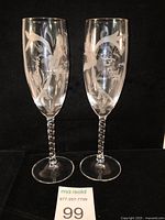 Pair of clear glass champagne flutes with twisted stems shown side by side against black background.