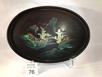 Oval black lacquer tray with detailed hand-painted landscape in gilt, red, light green, light brown tones, showing overall front view.