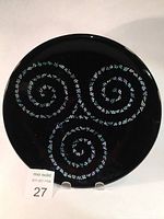 Full front view of a round black fused glass bowl with three iridescent spiral patterns forming a Celtic Triskel design.