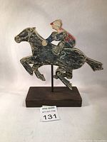 Front view of wooden folk art racing horse and jockey sculpture mounted on stand, showing worn paint and articulation.