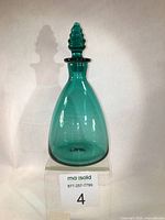 Full view of the teal green glass decanter showing cone-shaped bulbous base and stopper.
