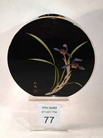 Front view of round black lacquer Ikebana vase showing hand-painted purple slipper orchids with gold trimmed leaves and artist inscription near base.