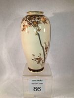 Front view of oval creamy vase decorated with brown and gold cherry blossom branch, showing artist's signature area near the base.