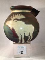 Front view of round raku-fired vase with white crackle glaze moose on dark iridescent background, showing raffia twine tied label.