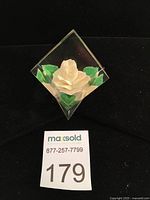 Front view of the Joseph Kulina lucite paperweight showing the carved white rose and green leaves inside a crystal clear lucite block.