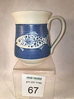 Front view of the stoneware mug showing blue background with salmon fish design, flared rim, and handle.