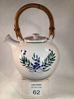 Front view of round white majolica glazed teapot with hand-painted blueberry design and bamboo handle.