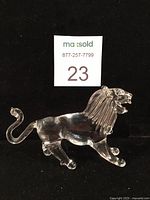 Clear hand blown glass lion figurine photographed on black background showing detailed mane, raised teeth, tail curl, and spurs on back legs.