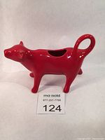 Red ceramic cow shaped creamer made by The Pioneer Woman, shown from side angle, highlighting glossy red glaze, cow head and tail loop handle.