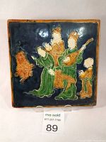 Front view of the square ceramic tile showing four musicians in sancai colors of green, ochre, and blue with glossy finish and clear relief details.