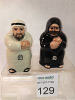 Front view of man and woman porcelain salt and pepper shakers on acrylic stand with numbered auction tag.