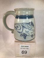 Front angle view of ceramic tankard showing hand-drawn salmon fish motif beneath a cobalt blue band.