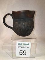 Front side view of Six Nations pottery cream jug showing carved geometric and leaf pattern on dark red stoneware body and blue glazed interior.