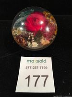 Front angle of the domed lucite paperweight showing vibrant red rose and other floral elements inside.