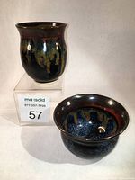 Photo showing both pottery pieces, a cup with a dark multicolor glaze and a matching bowl with similar glazing effects.