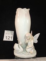 Front view of the vintage porcelain fairy and swan vase with pink daisy accents, showing the tulip-shaped vase, kneeling fairy, swan, and leaf base.