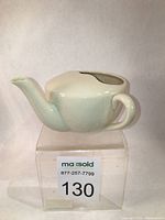 Side view of vintage porcelain feeding cup showing spout and handle, white to slightly green glaze.