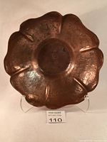 Front view of vintage hand hammered copper lotus flower bowl on a stand, showing patina and shape.