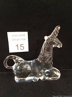 Clear glass unicorn paperweight shown from side on black background.