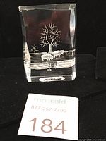 Front view of the clear acrylic lucite paperweight showing the reverse etched design of two bison grazing on grass with trees in the background.
