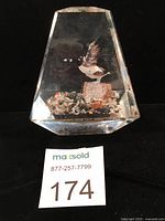 Front view of faceted clear lucite paperweight showing flying goose and standing goose on rock with gravel base.