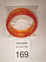 Wide domed vintage lucite bangle in honey amber and orange swirled butterscotch colors, displayed on a clear stand.