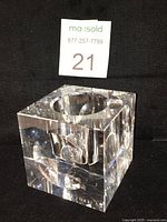 Clear square crystal votive candle holder with beveled edges and concave indents photographed on black background from an angled view.