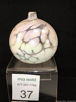 Front view of white iridescent glass bud vase or oil lamp with volcanic pattern on black background, sitting on clear acrylic stand.