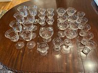 Full lot view showing all 29 pieces of antique-style etched glassware and stemware arranged on a wooden table.
