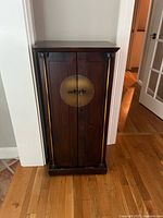 Front view of closed dark wooden cabinet with brass round handle in the center.