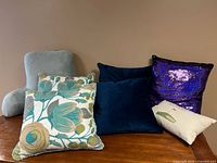 Set of 7 assorted decorative pillows including reading/backrest pillow, embroidered floral pillows, solid color pillows, reversible sequin pillow, and golf illustration pillow.