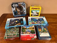 Overview of all puzzles in lot on table: Star Wars tin, Peanuts yellow box, two Ravensburger 200-piece puzzles, Kents Hill School box, ColorLuxe 500-piece, Rockefeller Center Christmas puzzle.