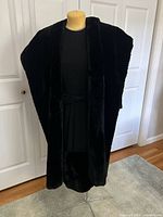 Full view of black fur-lined mid-length dress on dress form in front of white doors, showing the dress's shape and fur details.