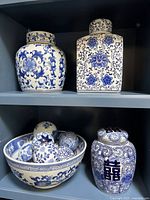 Four blue and white porcelain ginger jars displayed on shelves with a large decorated bowl holding porcelain spheres.