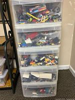 Stack of five transparent plastic bins filled with assorted LEGO pieces visible through drawers, showing mixed pieces of many colors and shapes.