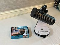Photo showing a Celestron branded tabletop telescope with a black patterned tube and adjustable eyepiece next to a boxed handheld digital microscope.