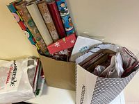 Photo showing multiple rolls of Christmas wrapping paper standing upright in a box, alongside some bags and tissue paper