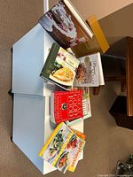 Top view of 6 out of 16 cookbooks stacked on white surface showing various cover designs and colors.
