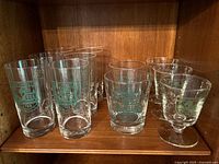 Group photo showing 11 assorted clear glasses with Dartmouth College green shield emblem on each, various shapes including tall, short, and stemmed glasses.