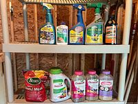 Shelf with various garden chemical spray bottles and fertilizer containers.