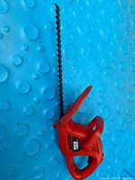 Side view of red Black & Decker electric hedge trimmer showing full blade and handle.